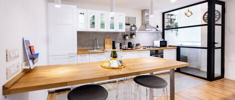 A modern kitchen with white cabinets, a wooden countertop, and bar stools.