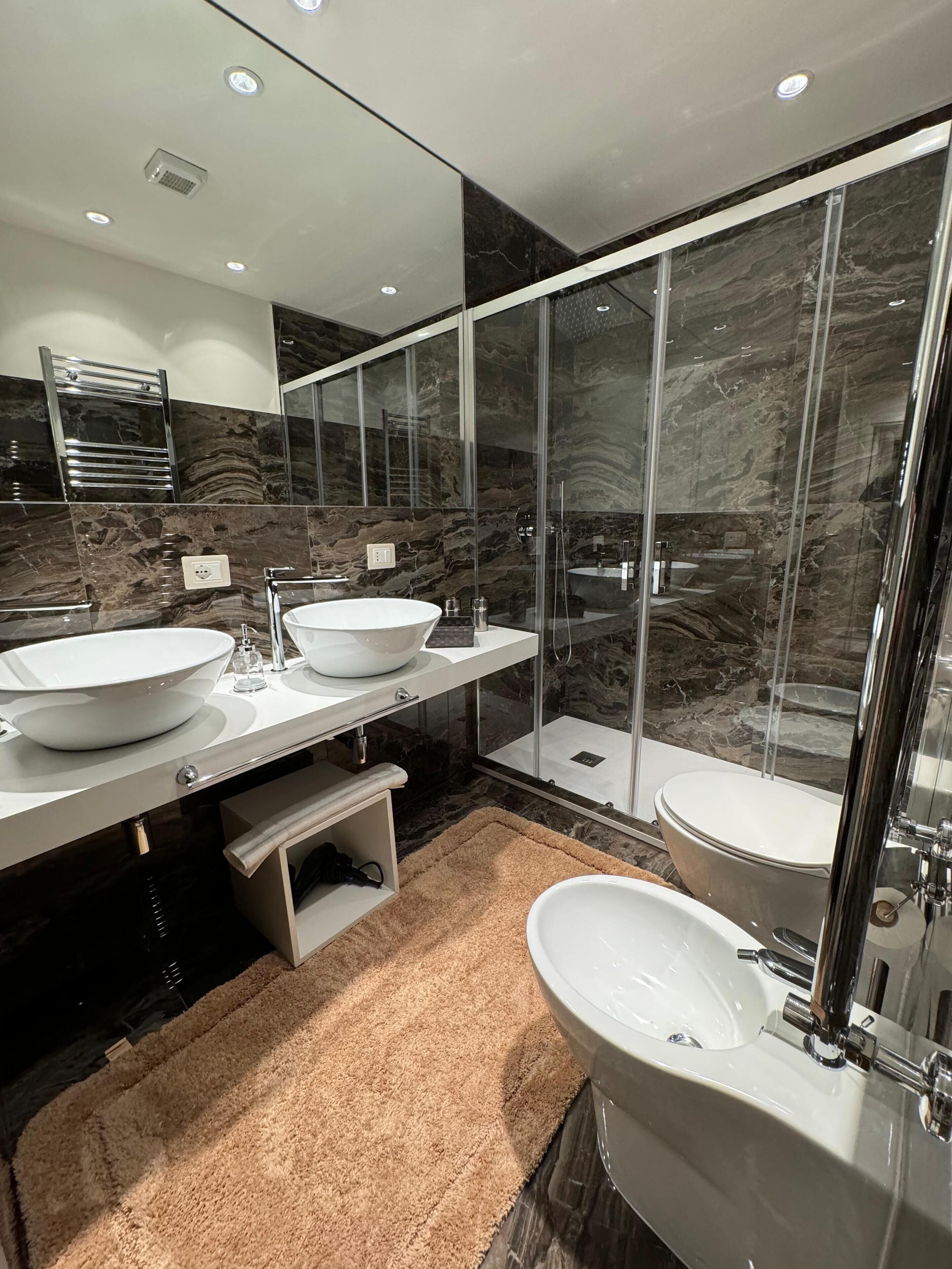 Ein modernes Badezimmer mit zwei Waschbecken, einer Duschkabine aus Glas und Marmorwänden.