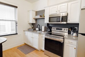 Una cocina compacta con armarios blancos, horno de acero inoxidable, microondas y cafetera.