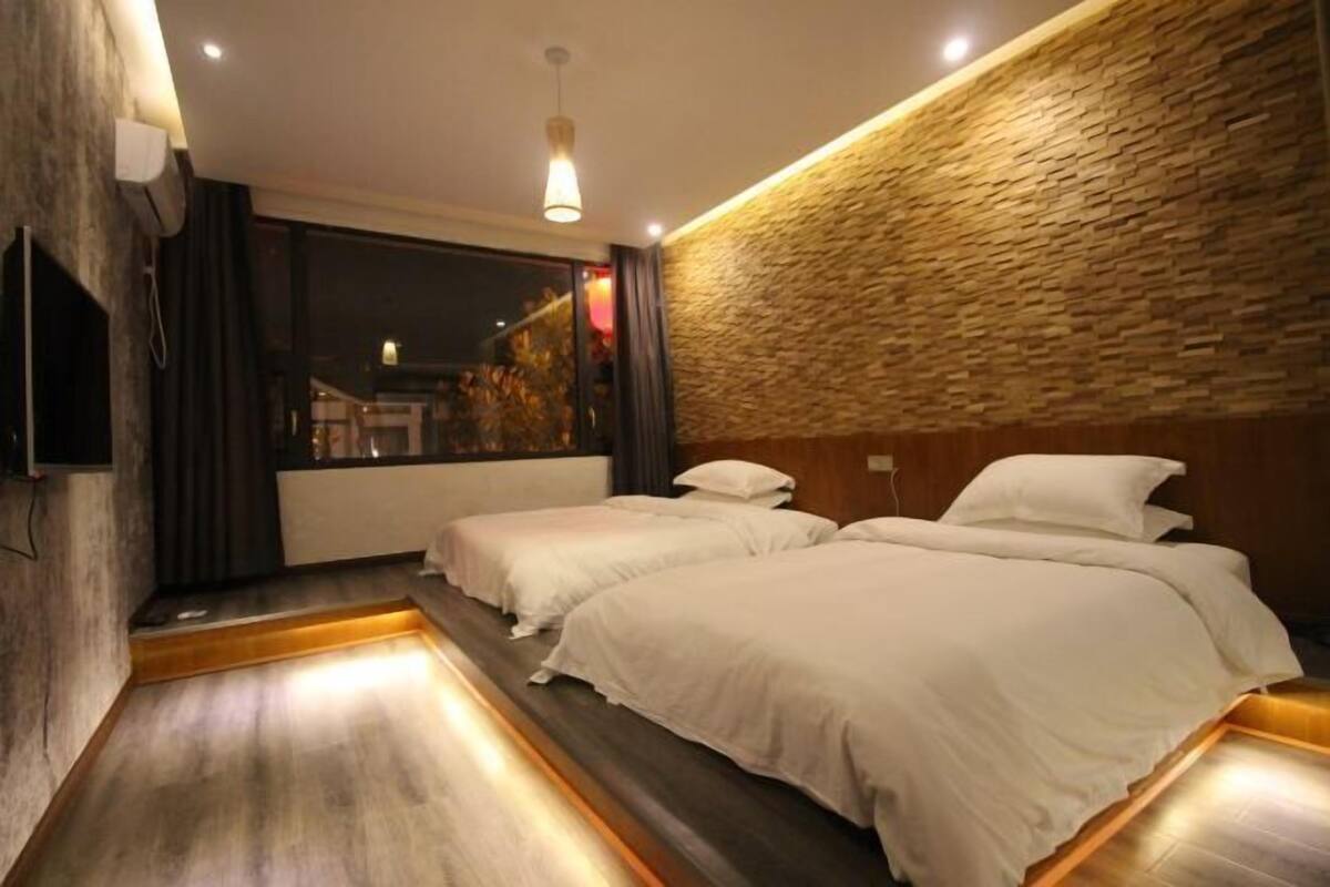 A hotel room with two beds, a stone wall, and a TV mounted on the wall.