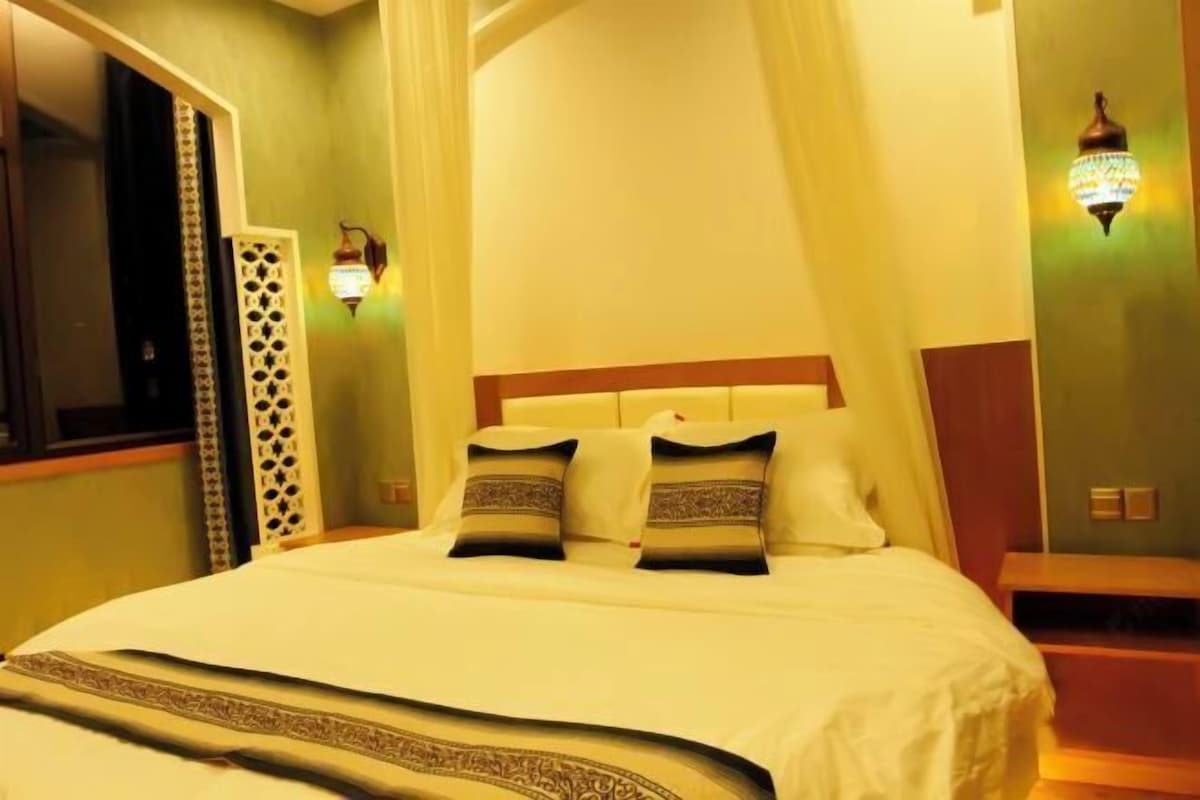 A neatly made bed with a canopy, two wall sconces, and a decorative screen on the left.