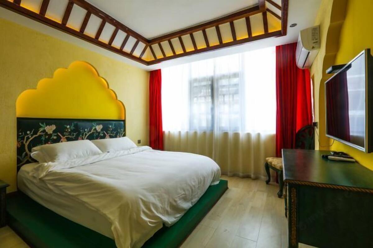 A hotel room with a bed, a television, a window with curtains, and a decorative ceiling.