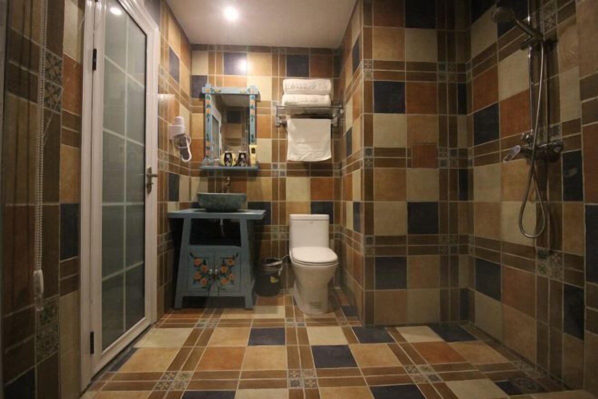 A bathroom with a tiled floor, a toilet, a sink with a mirror, and a shower area.