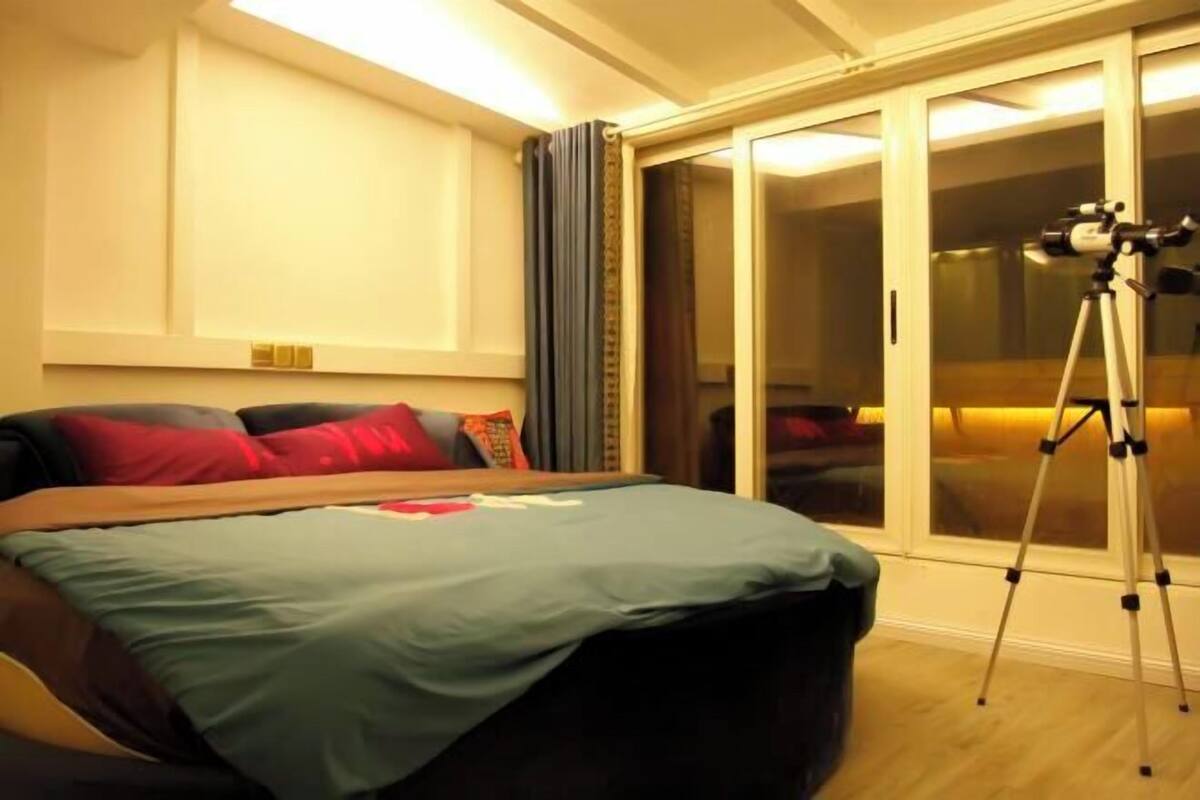 A bedroom with a bed, a telescope on a tripod, and a sliding glass door to the outside.
