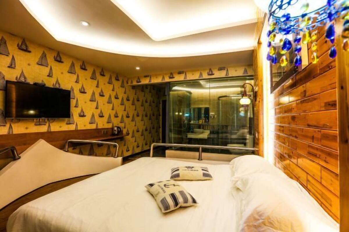 A hotel room with a bed, a television, a glass shower enclosure, and a wooden wall.