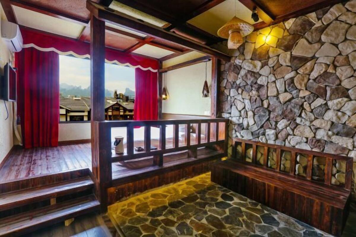 A wooden interior with a stone wall, a wooden bench, and a view through a window with red curtains.