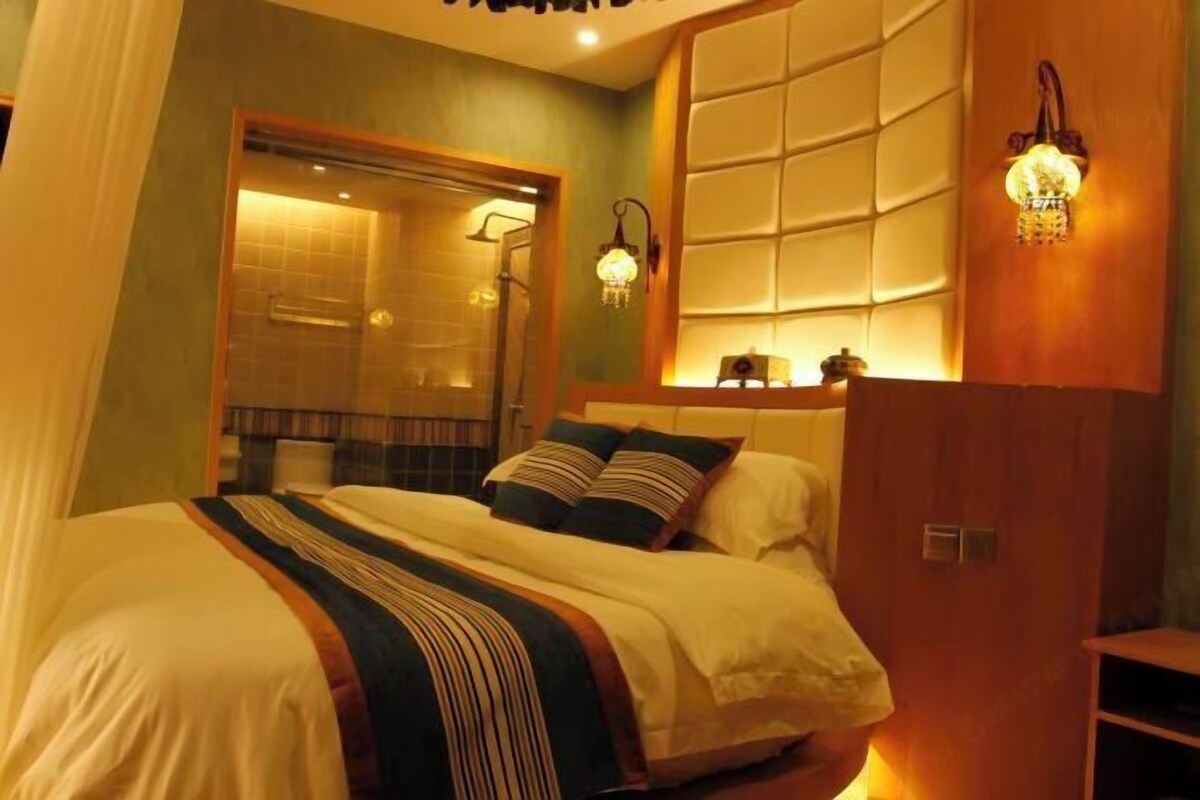 A hotel room with a large bed, a shower area, and a wall-mounted light fixture.