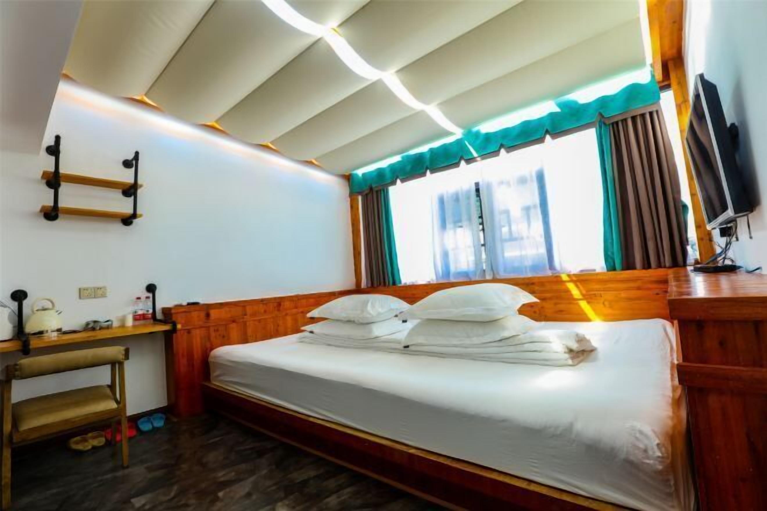 A compact hotel room with a wooden bed, a small desk, a television, and a window with curtains.