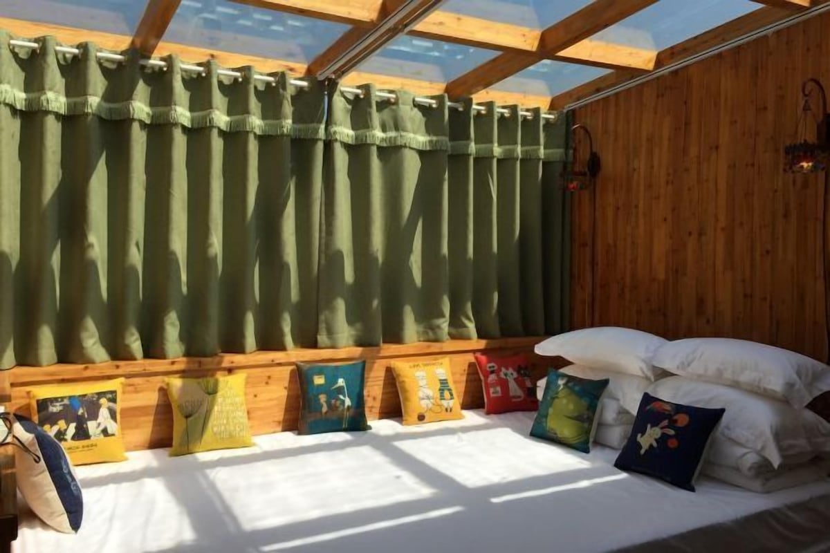 A room with a wooden ceiling, a skylight, a bed with white bedding, and colorful pillows.
