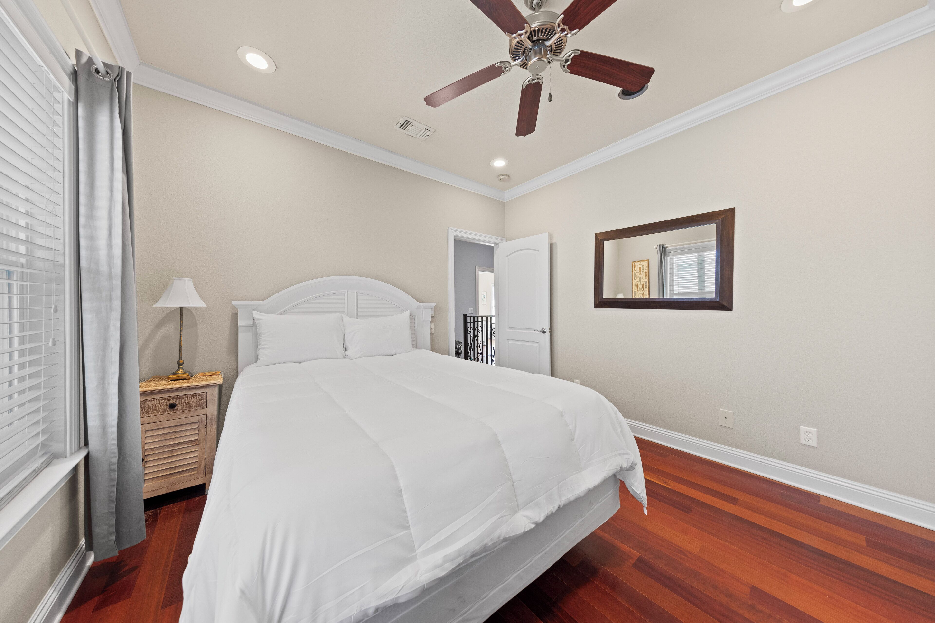 Une chambre à coucher avec un grand lit, un ventilateur de plafond, une table de chevet et une fenêtre avec des rideaux.