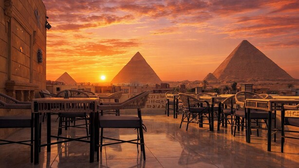 A rooftop terrace with a view of the pyramids at sunset.