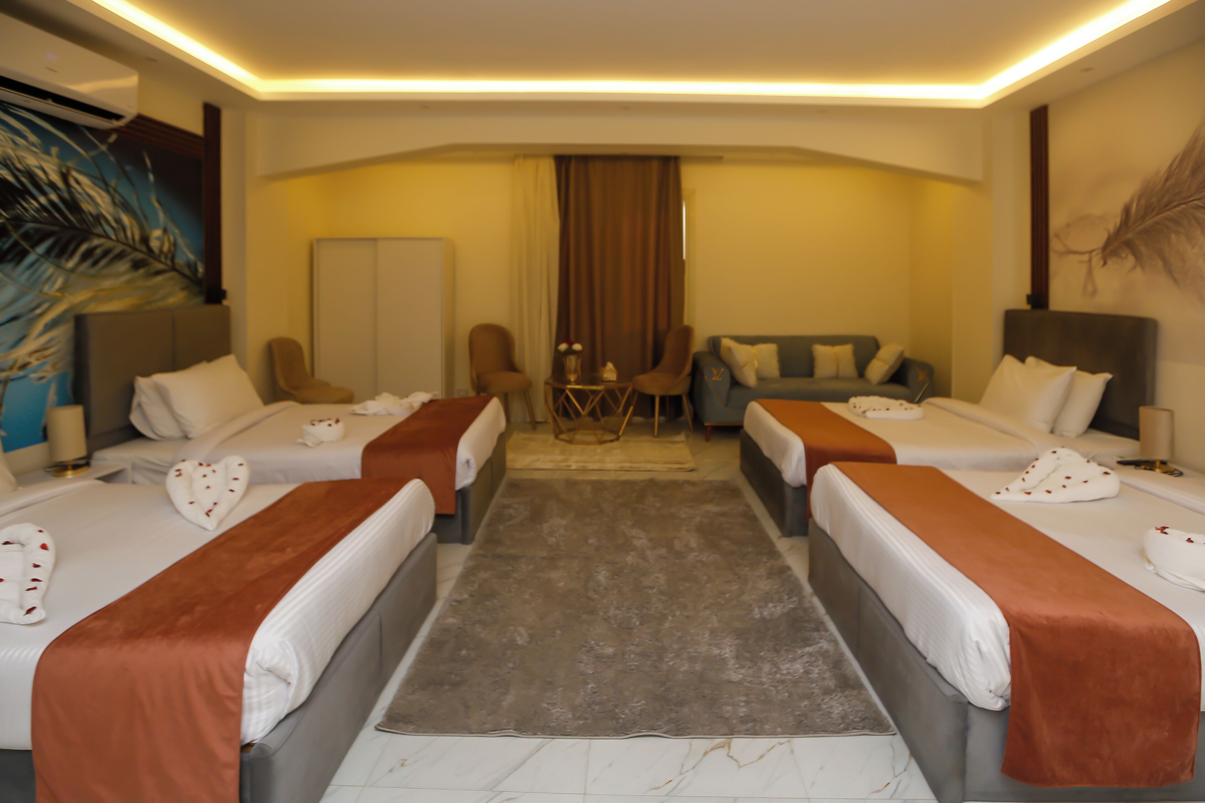 Habitación de hotel con dos camas, un sofá, una silla, una mesita pequeña y un adorno en la pared.