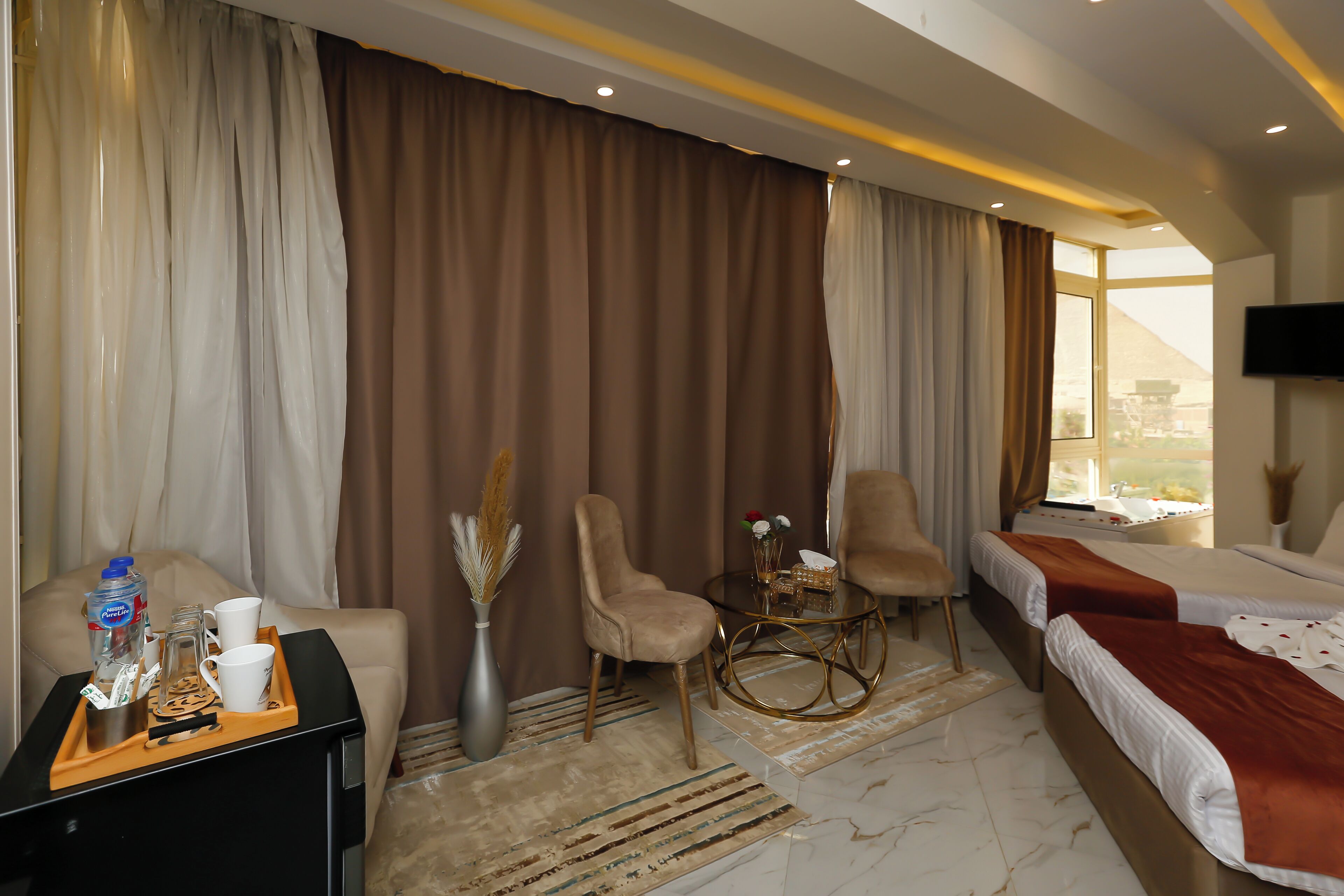 Habitación de hotel con cama, dos sillas, una mesita, televisión y ventana con vistas.
