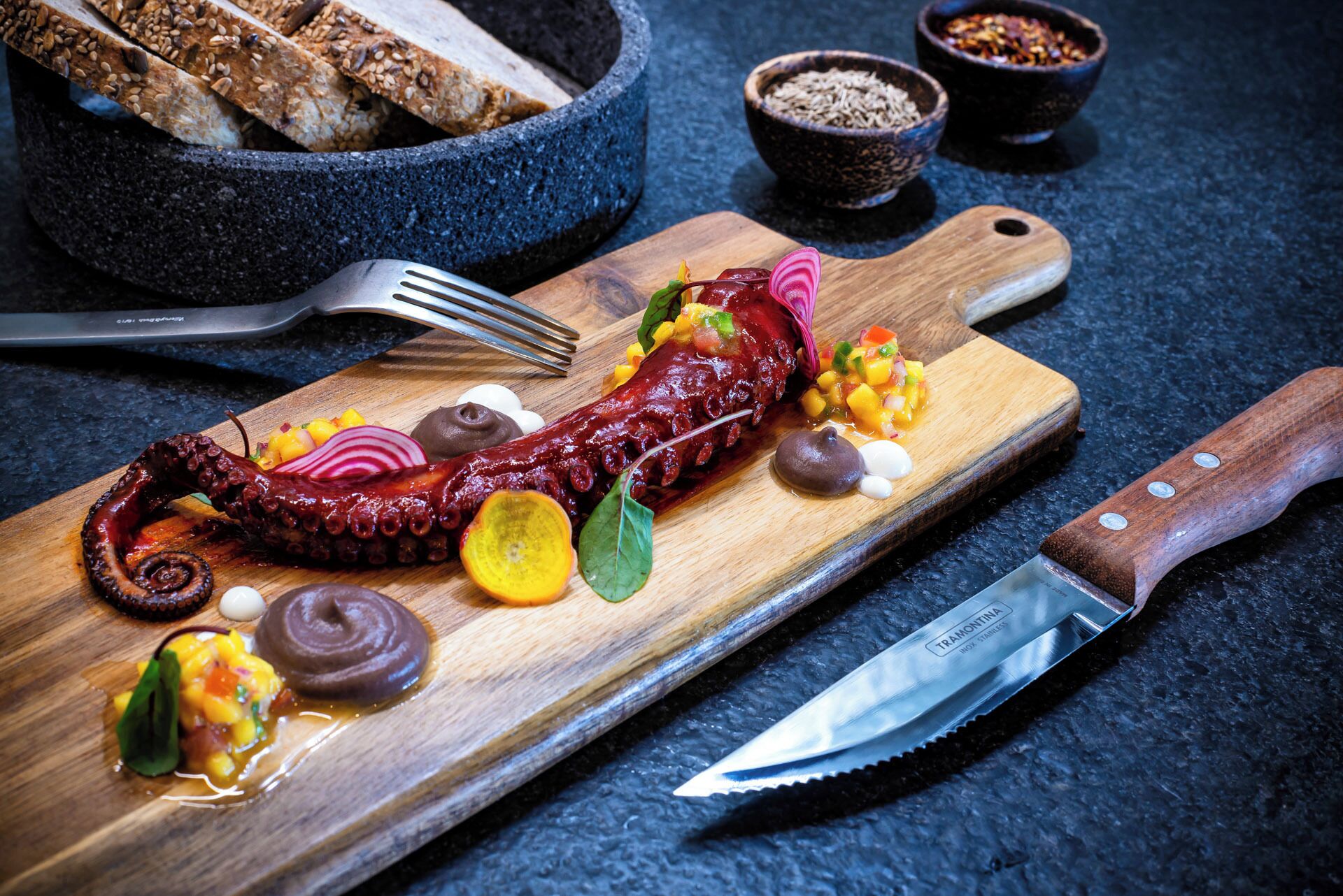 Una tabla de madera con pulpo, verduras y condimentos.