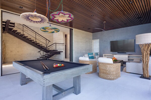 Una sala de estar moderna con una mesa de billar, muebles de mimbre, un televisor y una escalera.