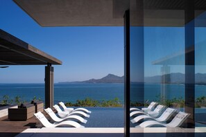 Un área de piscina moderna al aire libre con sillas de descanso y vistas al océano y a las montañas.