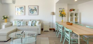 Un salon moderne comprenant un canapé, une table basse en verre, une table à manger avec des chaises et des œuvres d’art accrochées aux murs.
