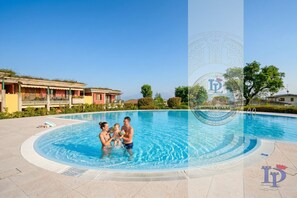 Una piscina con una familia, cielo despejado y un edificio con balcón.