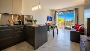 A modern kitchen with a central island, dining area with a table and chairs, and a sofa with red cushions.