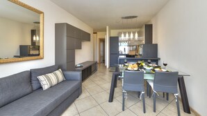 A modern living room with a grey sofa, a dining table with chairs, and a kitchen area in the background.