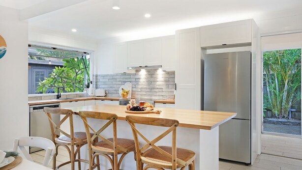 Eine moderne Küche mit weißen Schränken, einem Edelstahlkühlschrank und einer Holztheke mit Stühlen.