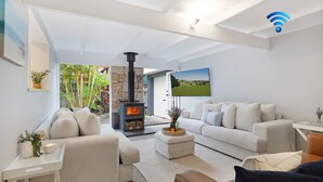 Ein modernes Wohnzimmer mit Kamin aus Stein, einem weißen Sofa, einem weißen Sessel und einem an der Wand befestigten Fernseher.