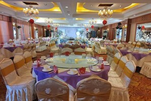 Un salón de banquetes con mesas redondas, sillas y un escenario.