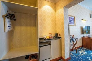 Habitación de hotel con un armario de madera, un refrigerador pequeño, una cafetera y una mesa con una bandeja de objetos.