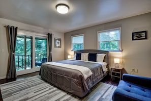 A bedroom with a large bed, two bedside lamps, a nightstand, a chair, and a view of the outdoors through a sliding door. - Creekside, spacious home for 8; 9 mi. Highlands, close Sky Valley, GA (Scaly Mountain)
