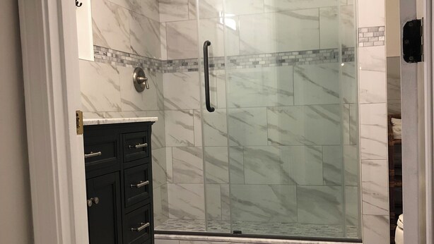 A modern bathroom with a glass shower enclosure, marble tiles, a dark wooden vanity, and a green rug. - Creekside, spacious home for 8; 9 mi. Highlands, close Sky Valley, GA (Scaly Mountain)