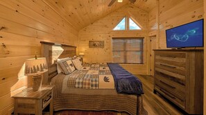 Une chambre confortable dans un chalet, avec un lit, une commode, un téléviseur et une fenêtre équipée de stores.