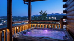 Un bain à remous sur une terrasse en bois, avec vue sur les montagnes et les bâtiments en arrière-plan.