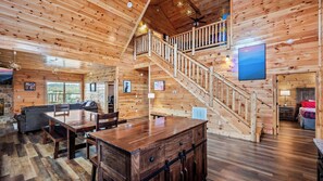 A wooden cabin interior with a dining area, a staircase, and a living room.