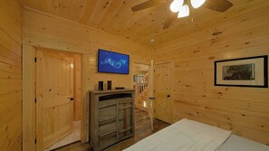 A wooden interior with a television mounted on the wall, a framed picture, and a wooden cabinet.