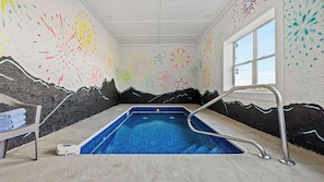 Une piscine dont les murs sont décorés d’une fresque représentant une montagne, avec une fenêtre et un porte-serviettes.