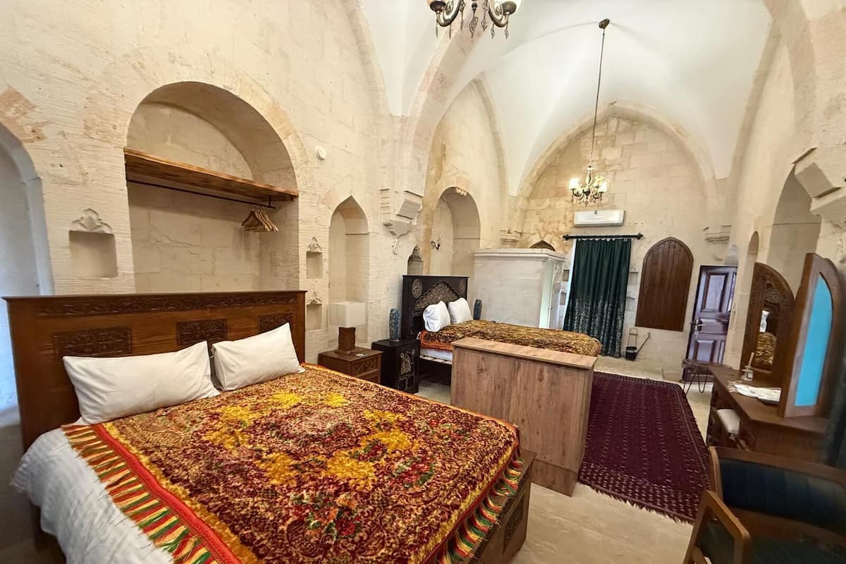 Ein Zimmer mit einem großen Bett, einem Nachttisch aus Holz, einem Schreibtisch und einem Stuhl. Das Zimmer verfügt über gewölbte Decken und Steinwände.