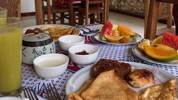 A table set with breakfast including toast, fruit, and beverages, with a view of greenery outside. - Jozani biosphere village  (Jozani)