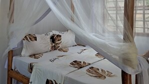 A bed with a canopy, a wooden headboard, and a window with a view. - Jozani biosphere village  (Jozani)