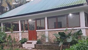A two-story building with a corrugated metal roof, large windows, and a stone facade. - Jozani biosphere village  (Jozani)