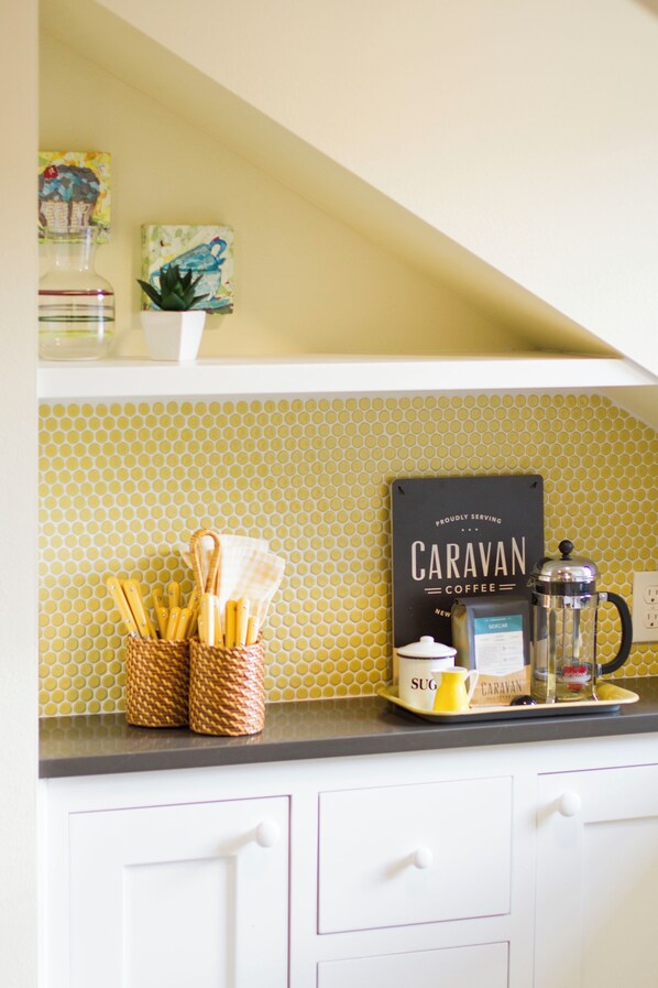 A kitchen counter with a coffee maker, sugar container, and a sign for Caravan Coffee. - Adorable attic cottage in the heart of Oregon Wine Country. (Newberg)