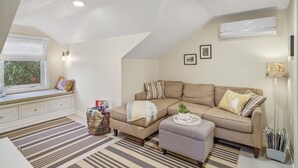 Een gezellige woonkamer met een bank, een voetenbankje en een vensterbank met uitzicht.