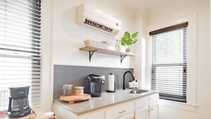 A kitchen with a coffee maker, a kettle, a sink, and a plant on a shelf.