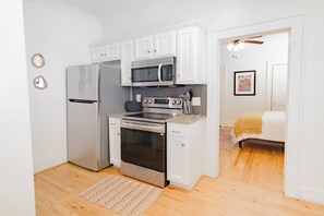 A compact kitchen with white cabinets, a stainless steel refrigerator, an oven, and a microwave. - Moroccan Dreams Suite, Walkable to Highland Park! (Birmingham)