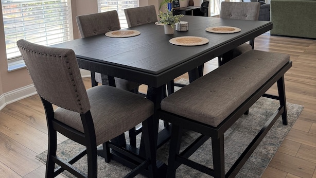 Comedor con una mesa de madera oscura, seis sillas, un banco y una lámpara colgante de fibras.