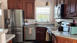 Una cocina con armarios de madera, electrodomésticos de acero inoxidable, una ventana con persianas y un tapete oscuro.