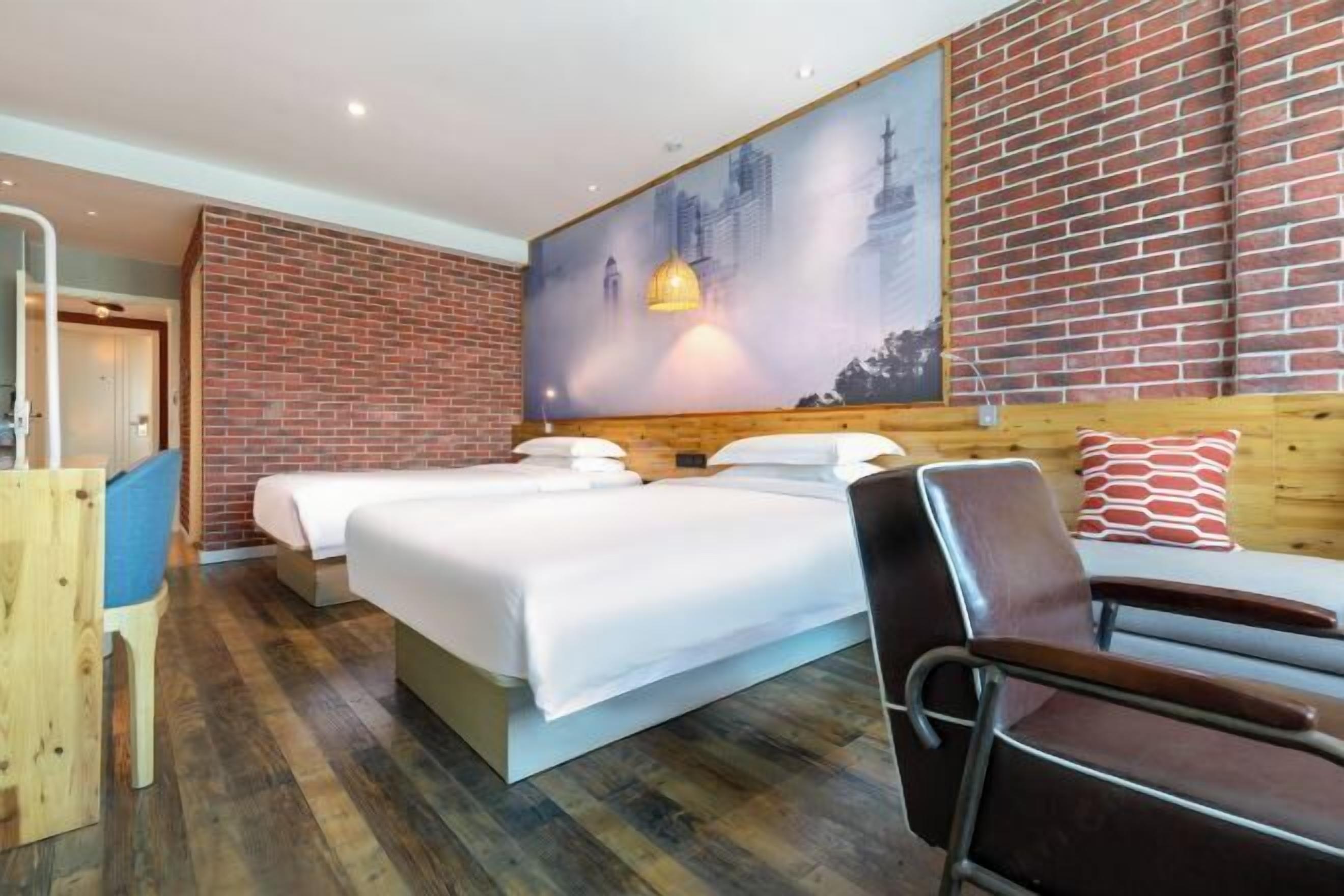 A hotel room with a brick wall, a large bed with white bedding, a wooden headboard, a wooden desk, and a chair.