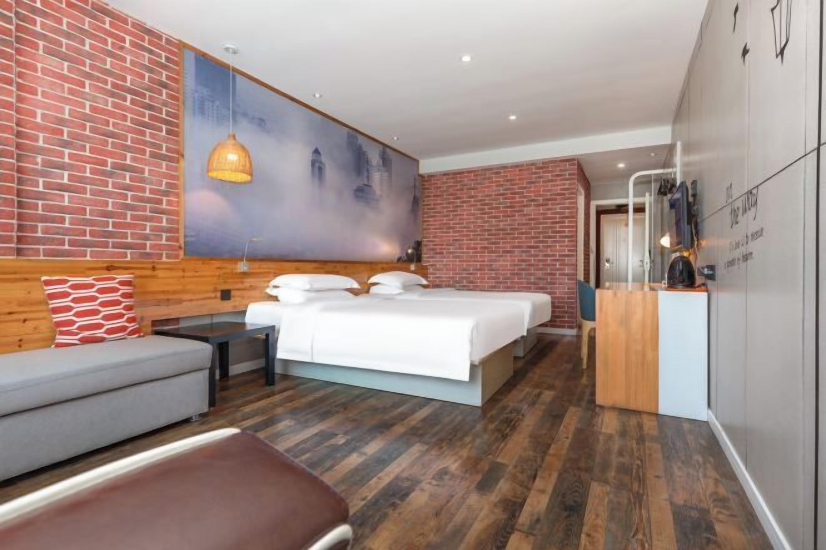 A modern hotel room with a brick wall, a large bed, a sofa, and a desk.