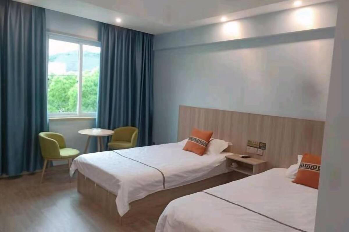 A hotel room with two beds, a small table, a chair, and a window with curtains.
