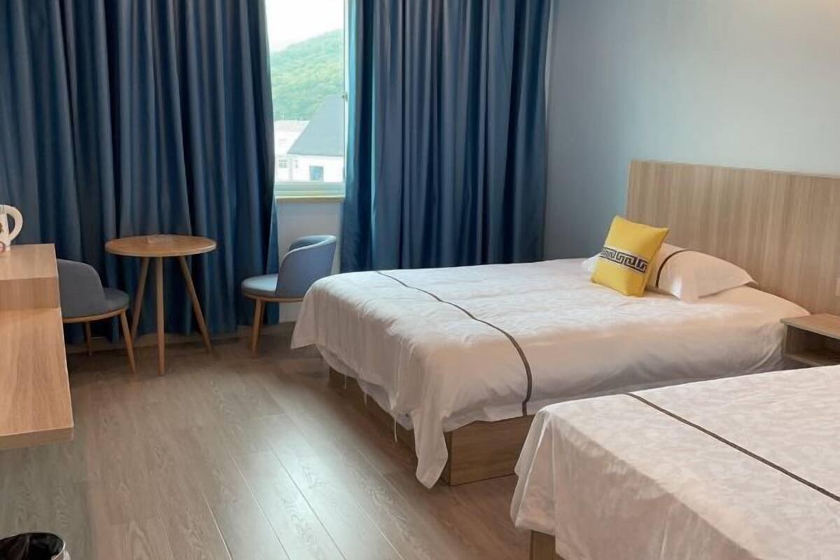 A hotel room with two beds, a desk, a chair, and a small table.