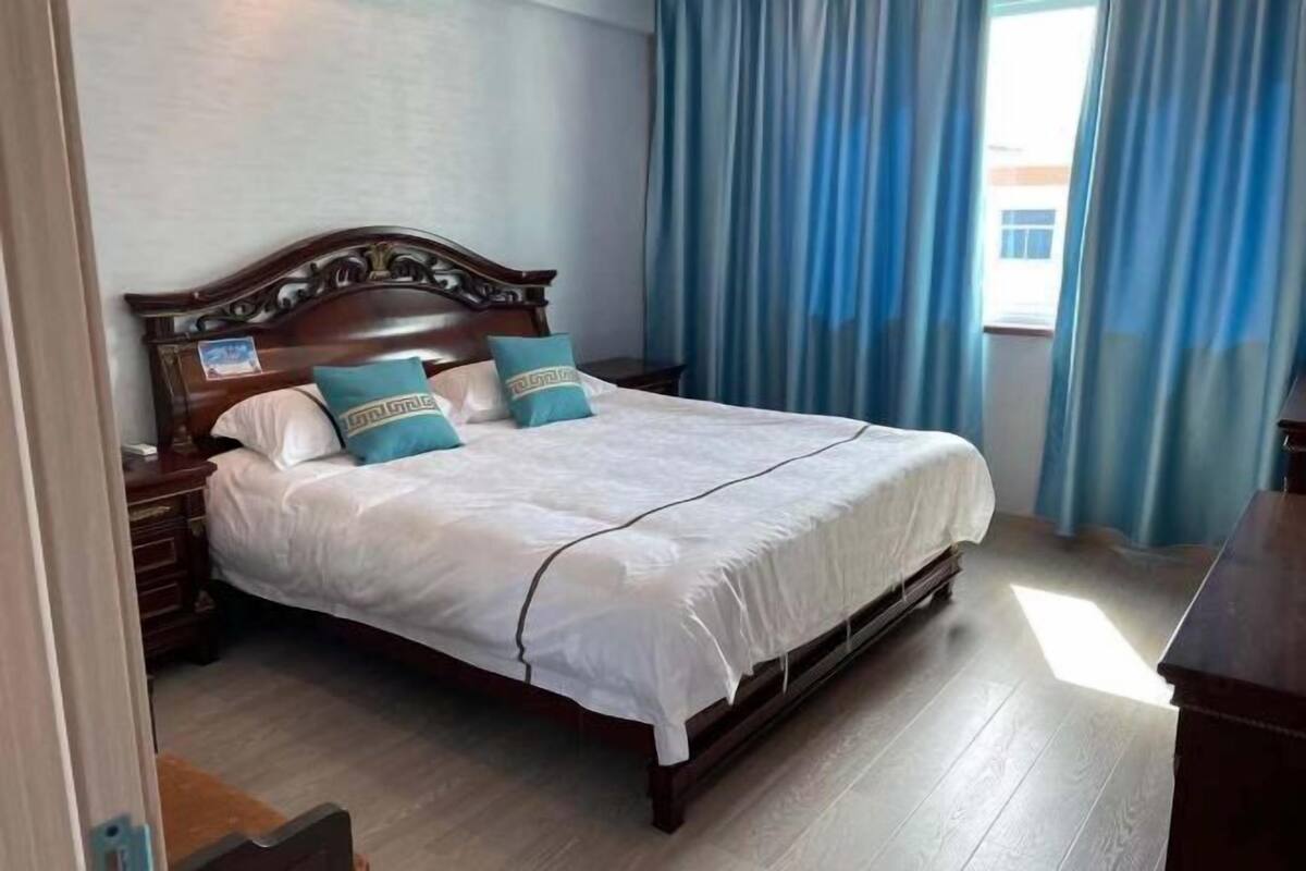 A neatly made bed with a wooden headboard, a nightstand, and a window with blue curtains.